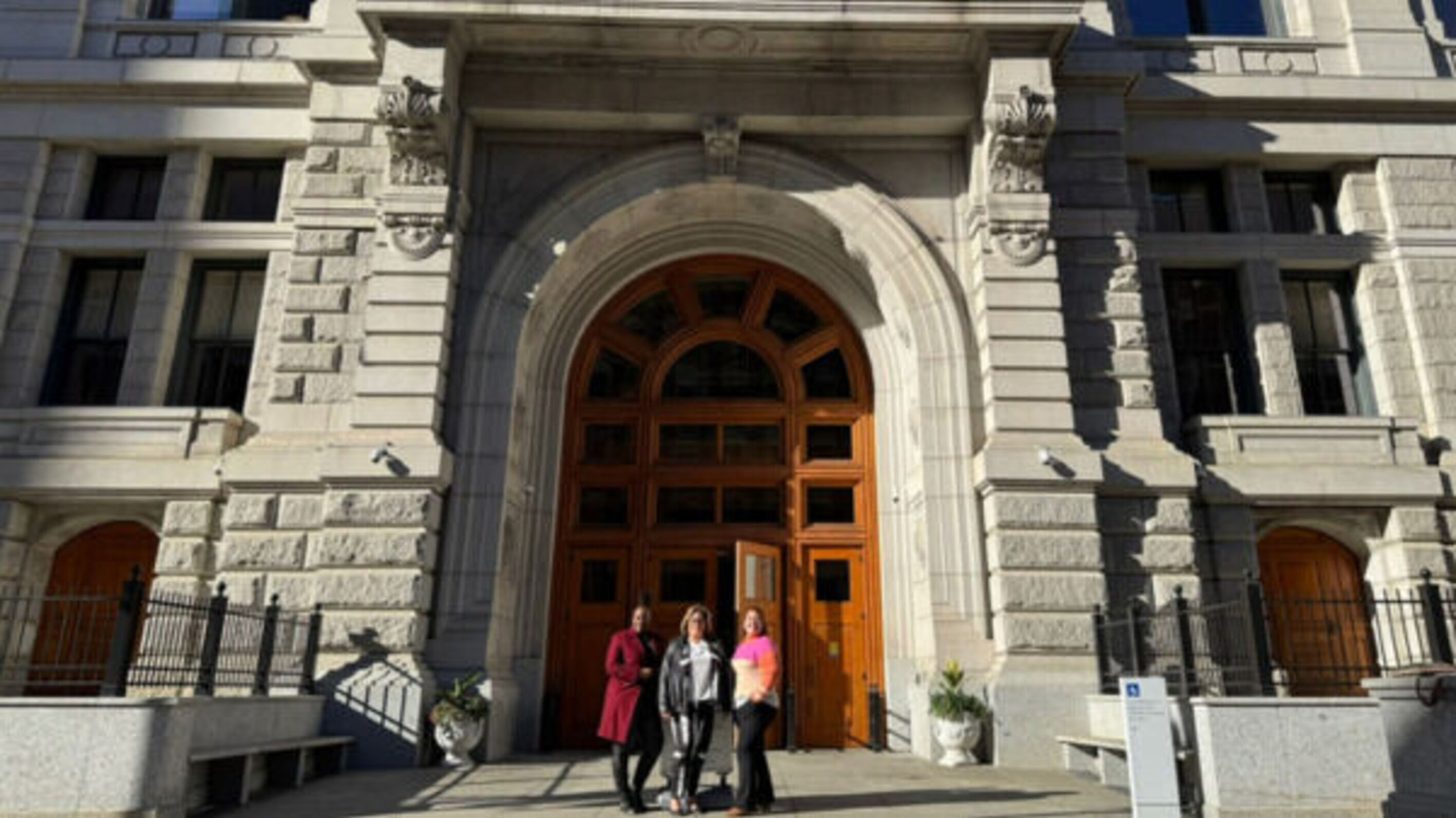 Three women stand in front of a large, ornate entrance of a historic building.